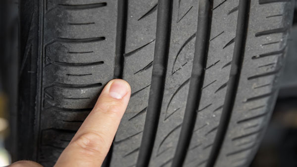 Image of a car tyre with a finger pointing on the area where it shows very low tyre tread depth which is illegal in the UK